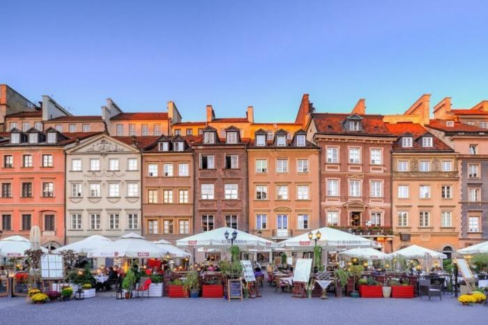 A picturesque view of Warsaw's Old Town Market Square, featuring colorful historic buildings with outdoor restaurants and cafes. A popular destination for tourists, including those visiting Poland for dental tourism.