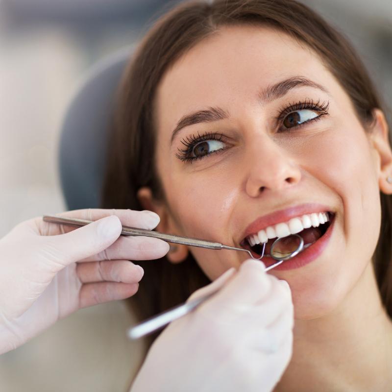 A smiling woman receiving a dental check-up, with a dentist using a mirror and probe to examine her teeth. The image highlights professional dental care, possibly related to dental tourism or cosmetic dentistry.