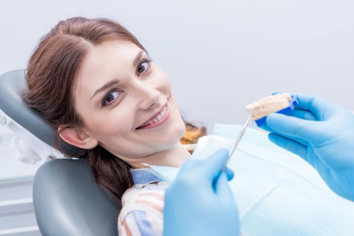 A smiling female patient sitting in a dental chair while a dentist wearing blue gloves prepares a dental impression, highlighting a positive dental care experience.