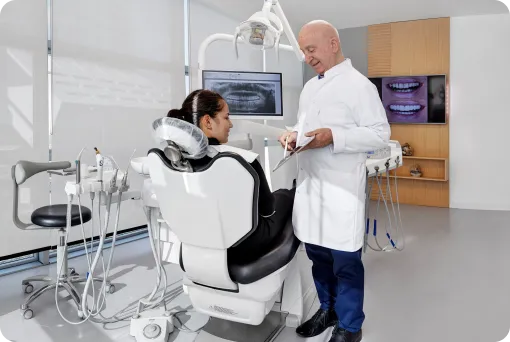 A female dentist wearing a mask and gloves prepares for a procedure with a patient in a modern clinic.