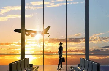 A traveler standing in an airport terminal, looking out at an airplane taking off during a sunset. The image represents travel, possibly related to dental tourism or medical tourism abroad.