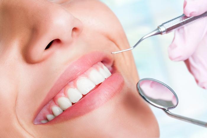 A close-up of a smiling woman receiving a dental check-up. A dentist wearing gloves uses dental tools to examine her teeth, emphasizing professional oral care and cosmetic dentistry, often sought in dental tourism.
